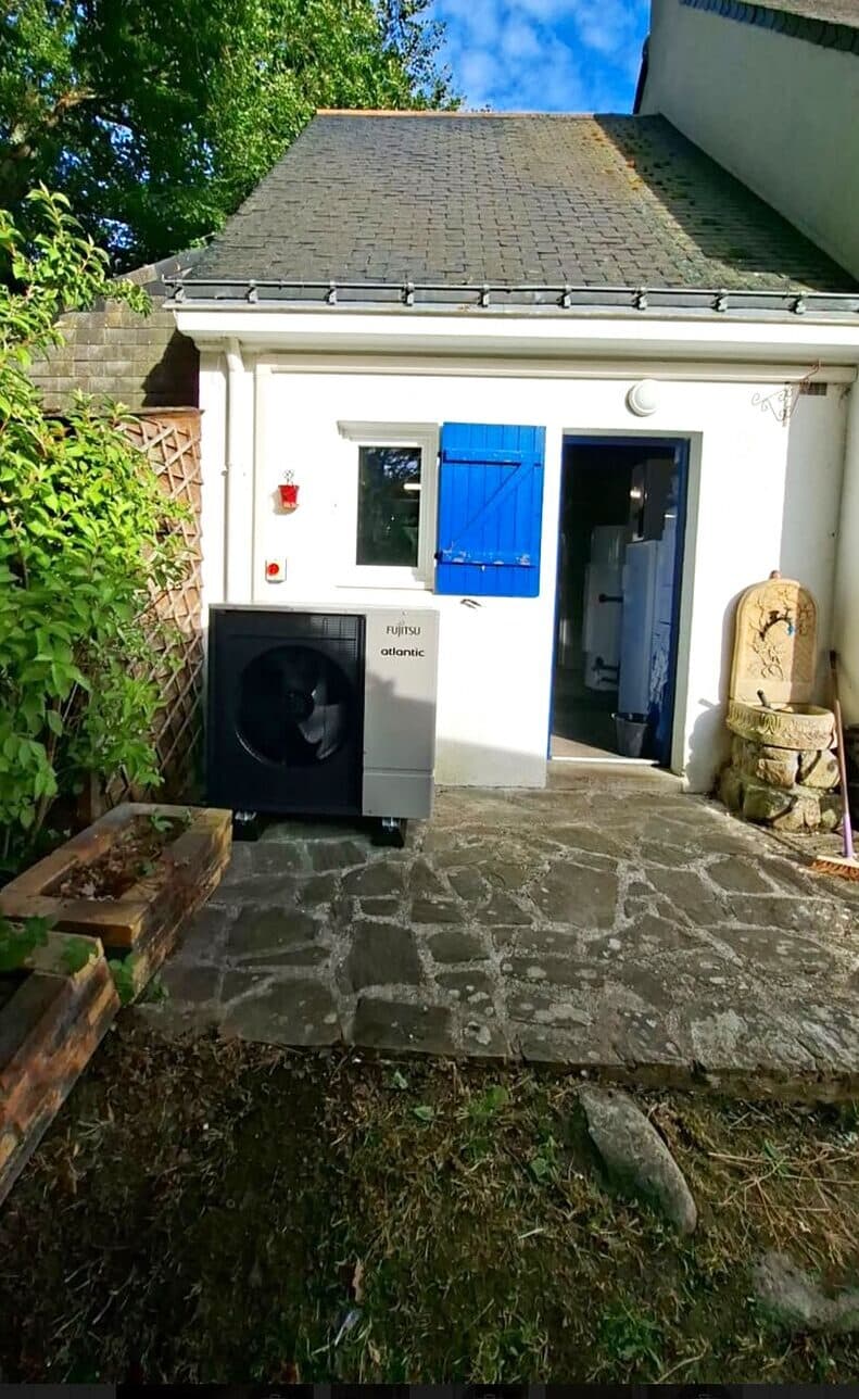 Pompe à chaleur installée dans la cour d'une maison aux volets bleus
